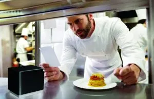 Chef in modern, professional kitchen looking at ticket from mC-Print3 thermal receipt and restaurant printer by Star Micronics.